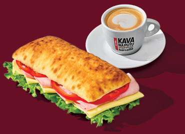Sendvič Royal u ciabatti sa šunkom, sirom, rajčicom i zelenom salatom te šalica kave espresso na tamnocrvenoj podlozi.