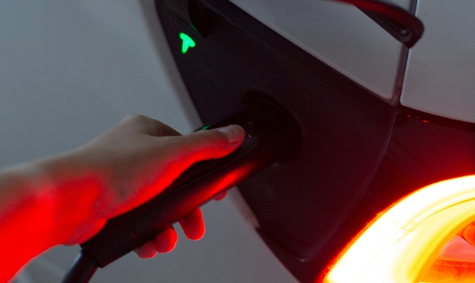 Na slici je prikazana ruka koja priključuje kabel za punjenje u električno vozilo.