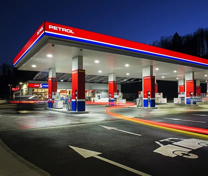 Petrolovo prodajno mjesto noću s osvijetljenim točionicama, trgovinom i svjetlosnim tragovima vozila.