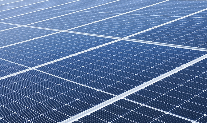 Na slici su fotonaponski solarni paneli postavljeni u pravilnim redovima. Paneli prekrivaju veliku površinu i prikazani su iz blizine, s jasno vidljivom mrežom fotonaponskih ćelija.